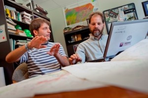 Alec Bernstein '11 talks David Brandes, who is sitting behind a laptop computer in his office.