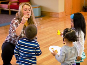 A student blows bubbles with three children.