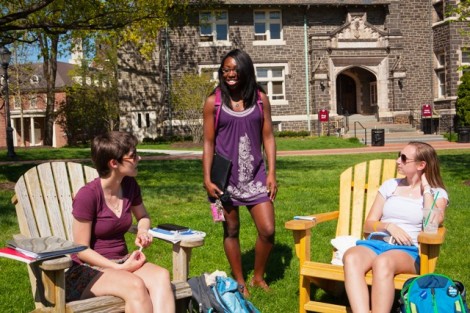 Emily Bennett '16 (L-R), Brandi Porter '13, and Liza Fryman '16 talk on the Adirondack chairs in front of Hogg Hall.