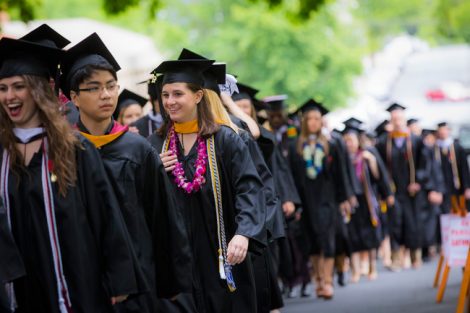 Students wearing their caps and gowns stand in line on the way to Commencement.