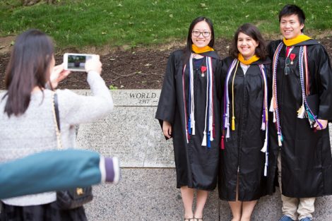 Three graduates pose for a photograph in front of a war memorial