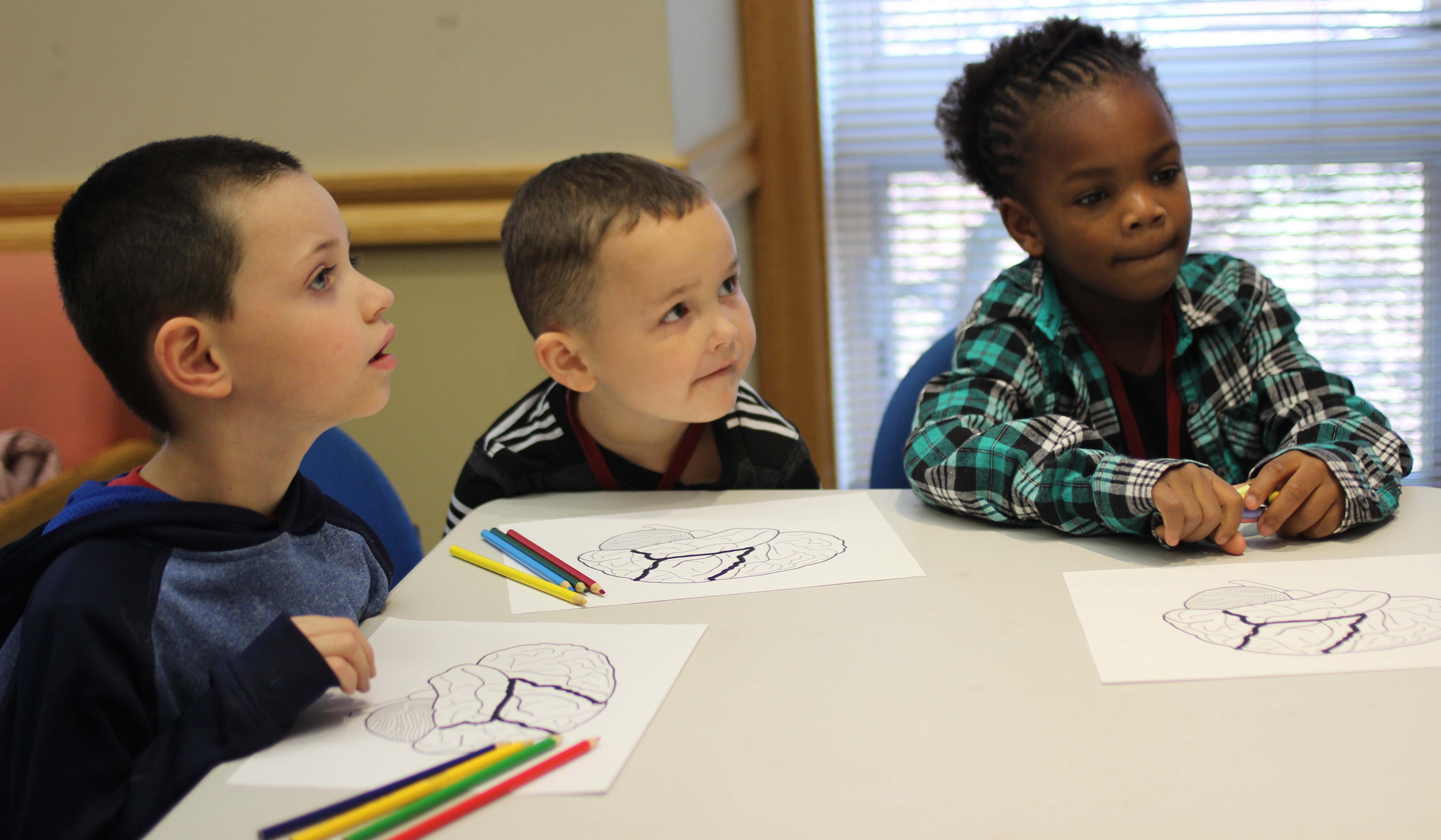 Three young students sit at a table and listen to what's taught.