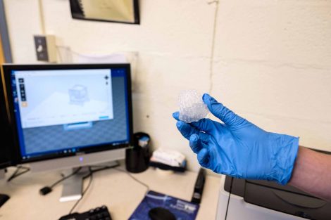 Someone with a glove holds a small item created with a 3D printer.