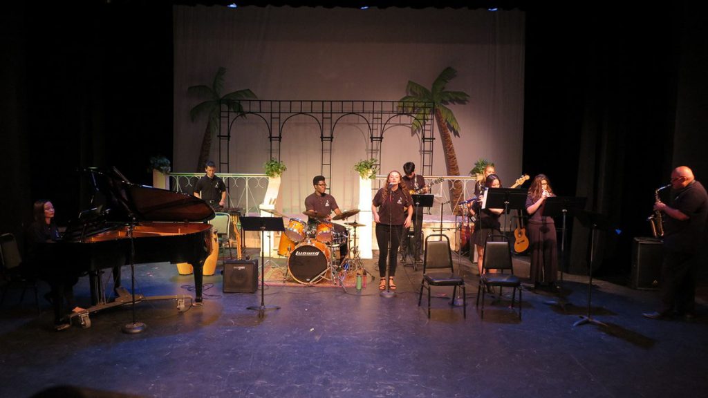 Michael Anekwe plays drums in a band performing on stage.