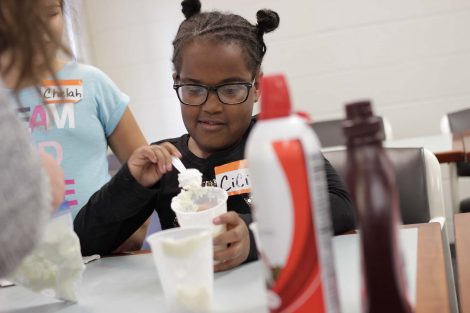 Student adds whipped cream to her ice cream.