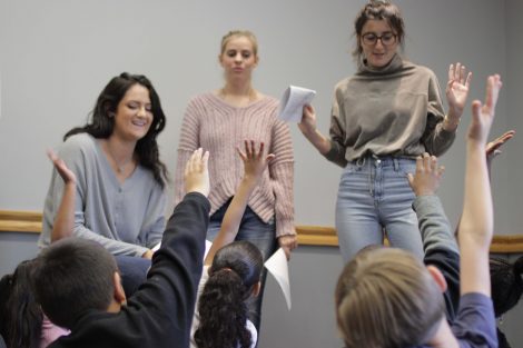 Elementary students raise their hands.