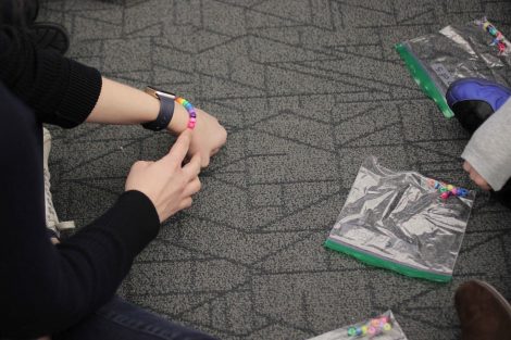 Elementary students see the beaded bracelet they will make after sharing beads.
