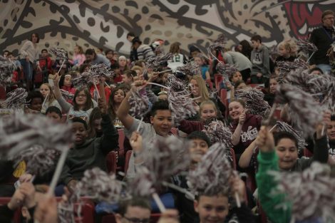 Boy smiles as he shakes his pom pom and chants.