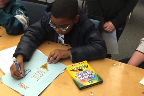 A child uses magic marker to draw a picture on paper.