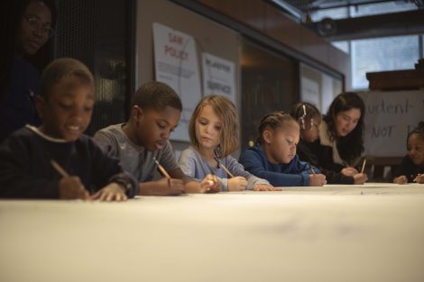Kindergartners line the tables getting ready to draw on them.