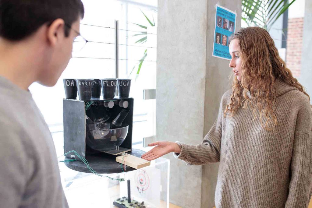 Female student explains how the baking machine works to another classmate.