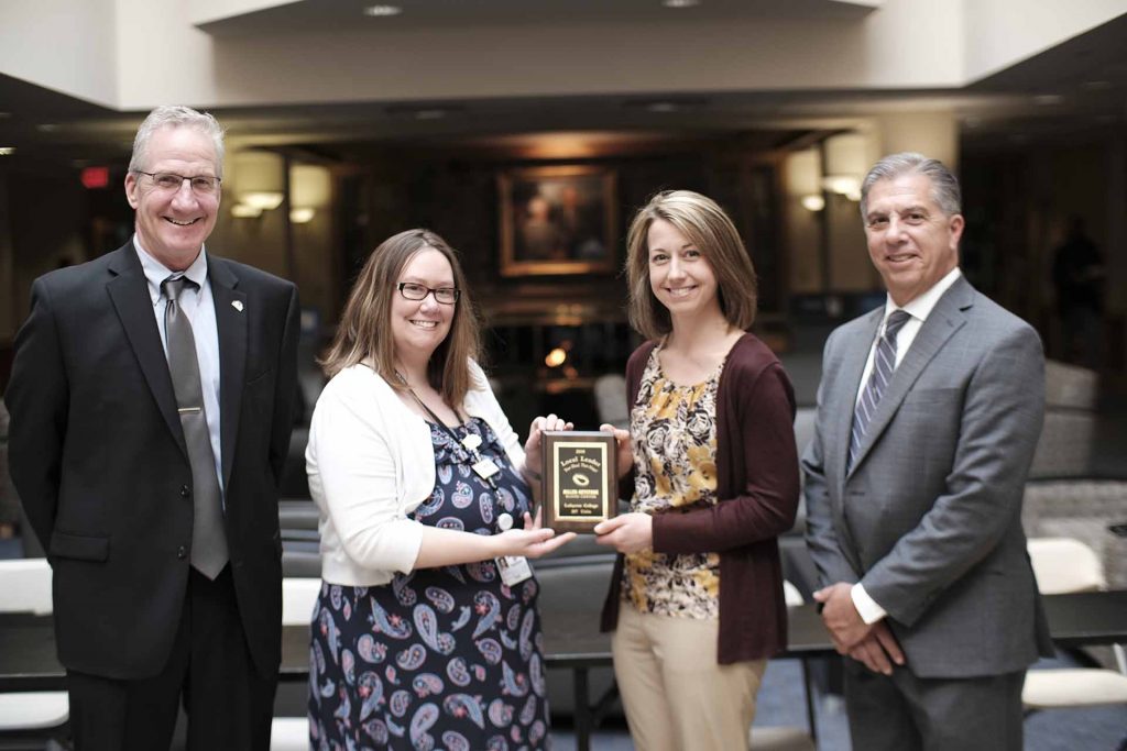 Amber Zuber receives a plaque from Miller-Keystone Blood Center leaders Michael McShane, Krista Hill, and Pete Castagna.