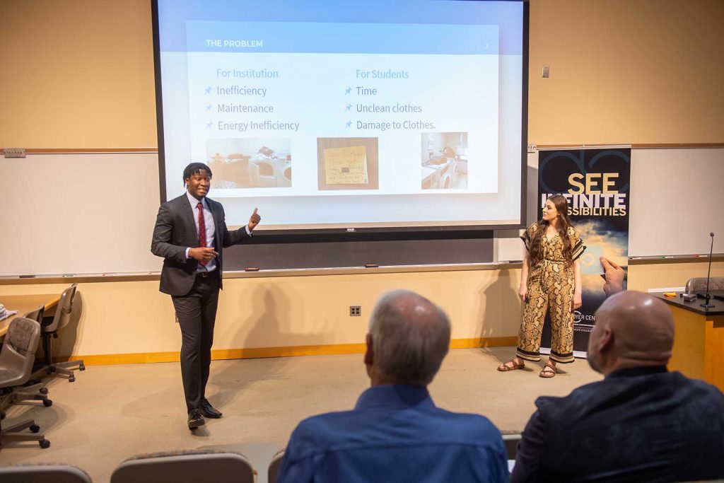 Michael Anekwe ’22 and Serena Fenaroli ’22 stand before a screen and present their business idea.