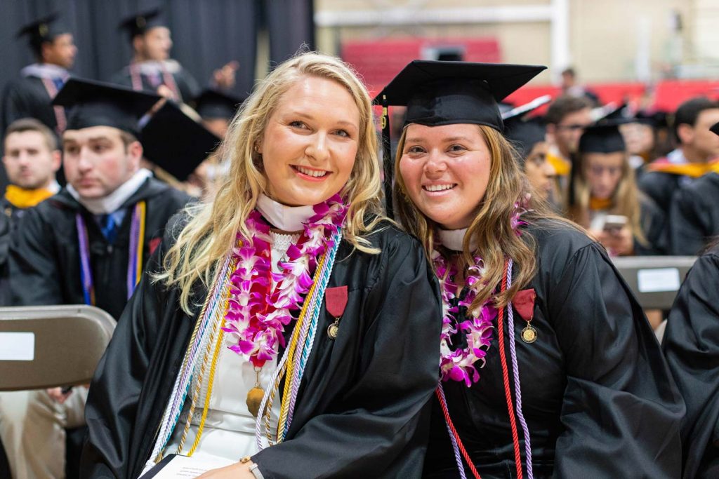 Reeve Lanigan '19 sits in her Commencement gown and poses for a photo with a classmate.