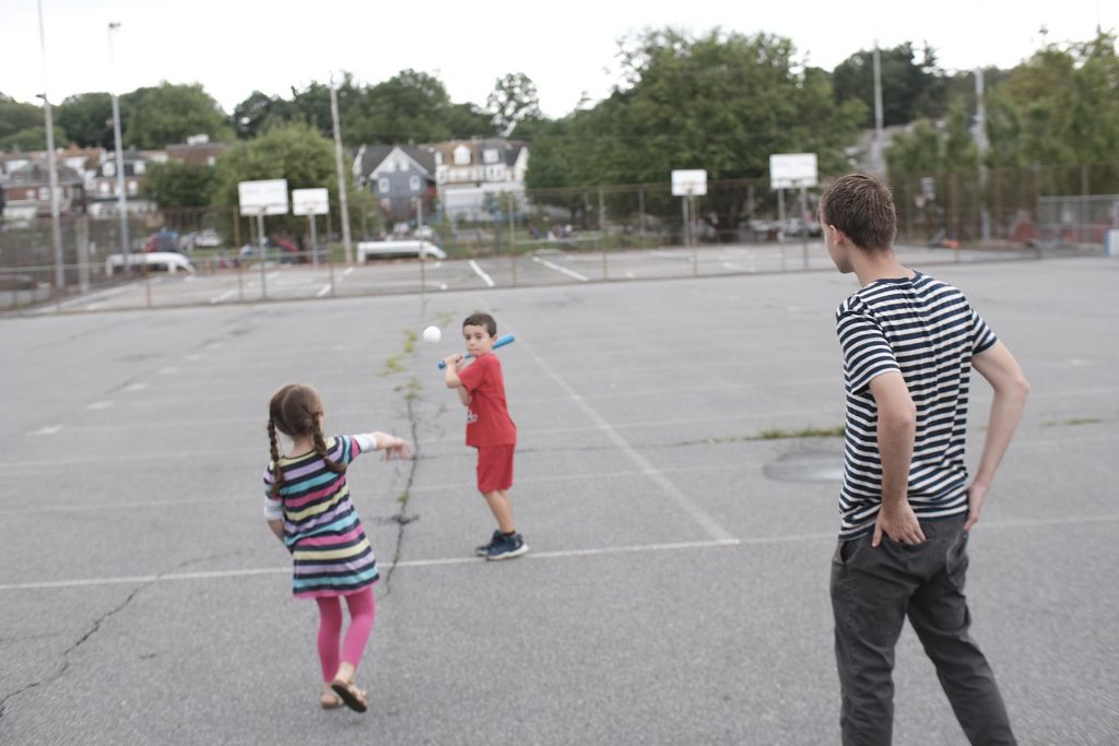 Girl pitches a wiffle ball to her brother as a Lafayette student watches.