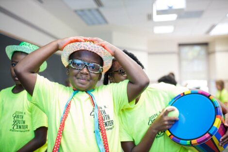 One kids in the community smiles while wearing a fun hat