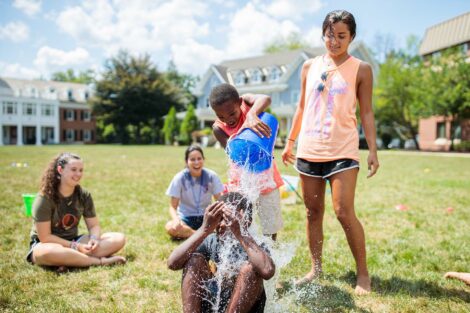 One kid in the community pours a bucket of water on another kid's head