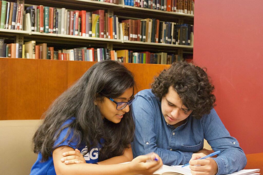 GoPeer tutor helps a student as they lean over a book and papers.