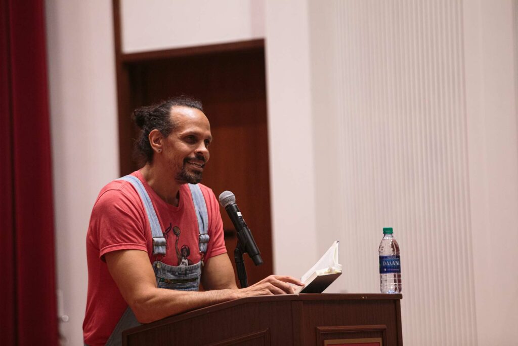 Ross Gay '96 stands at a lectern and speaks with a crowd at Colton Chapel 