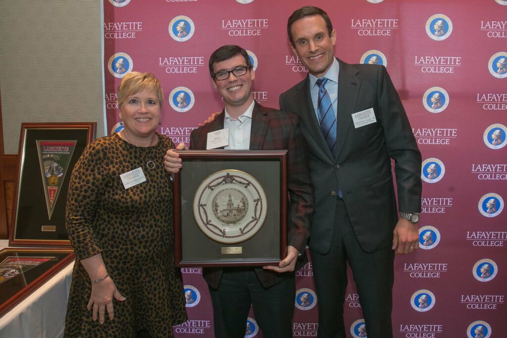 Matt holds framed award and is flanked by alumni relations director and president