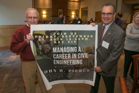 John Pierce holds a poster on one side while Professor Dave Veshoski