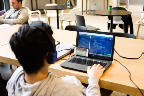 a student sits in front of a laptop coding and watching football