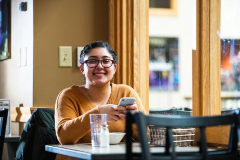 A student sitting at a table smiles for the camera on the first day of spring semester.