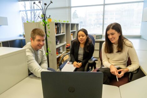 Student externs sit at desk with host who shows them something on a computer