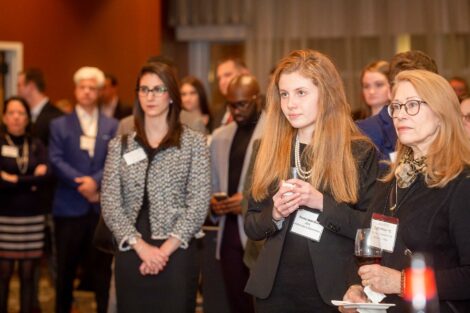 Students, alum, and staff listen as host speaks the the podium