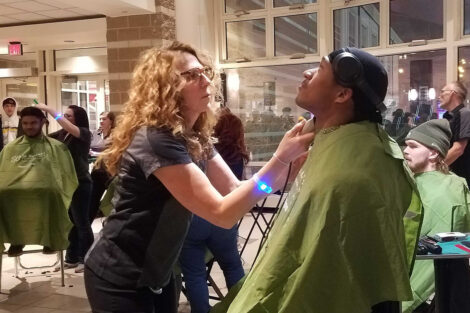 A large group of students gather in Kirby Sports Hall to watch as fellow students get their heads shaved for a cancer charity.