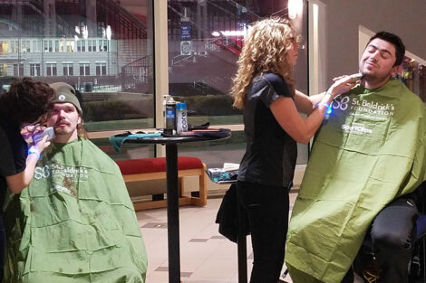A large group of students gather in Kirby Sports Hall to watch as fellow students get their heads shaved for a cancer charity.