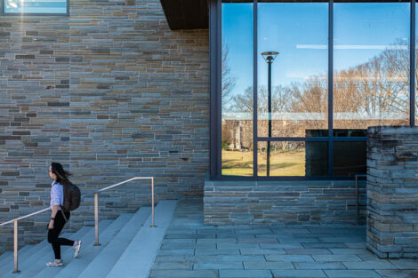 A student with rolled up sleeves leaves Skillman Library on an unseasonably warm day in Winter.
