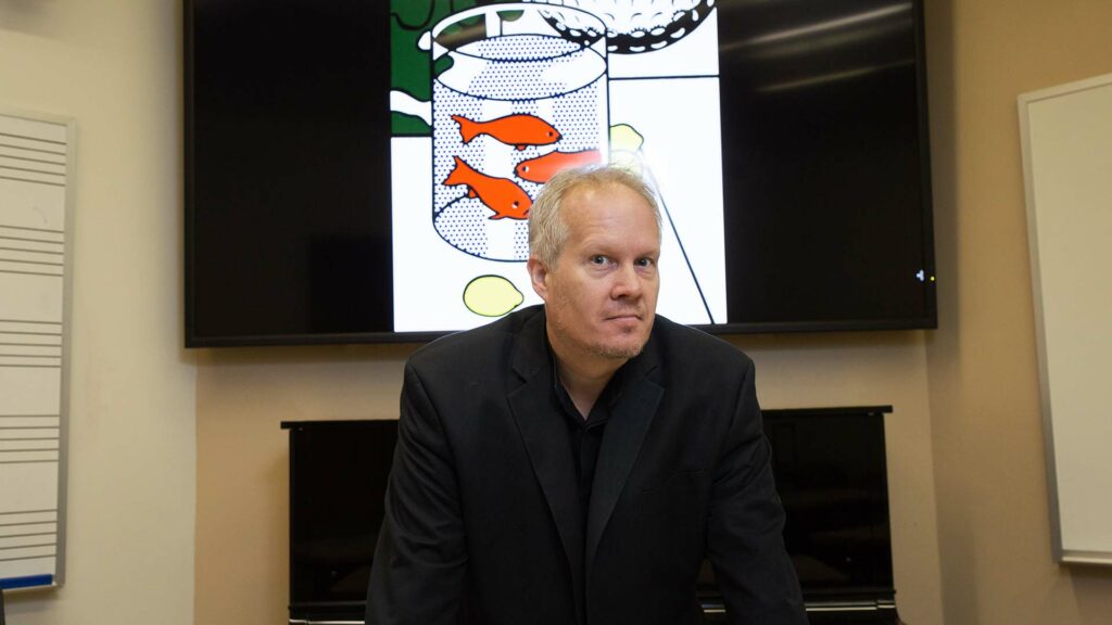 Kirk O'Riordan standing in classroom in front of piano and artwork