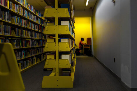 A student, in a mask, studies behind a bookshelf.