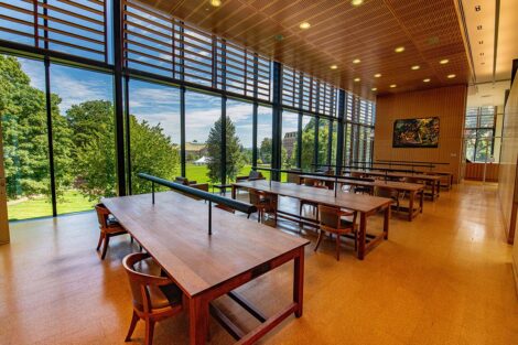 A row of empty tables in front of a window showing the Quad, inside of Skillman Library