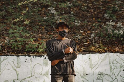 Habib Fall poses with his paintbrush in front of mural