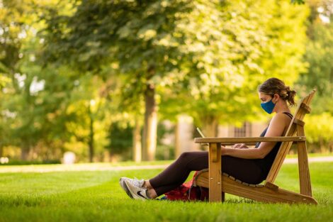 student reads in a mask on the Quad