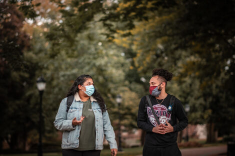 two students wearing masks walk on campus