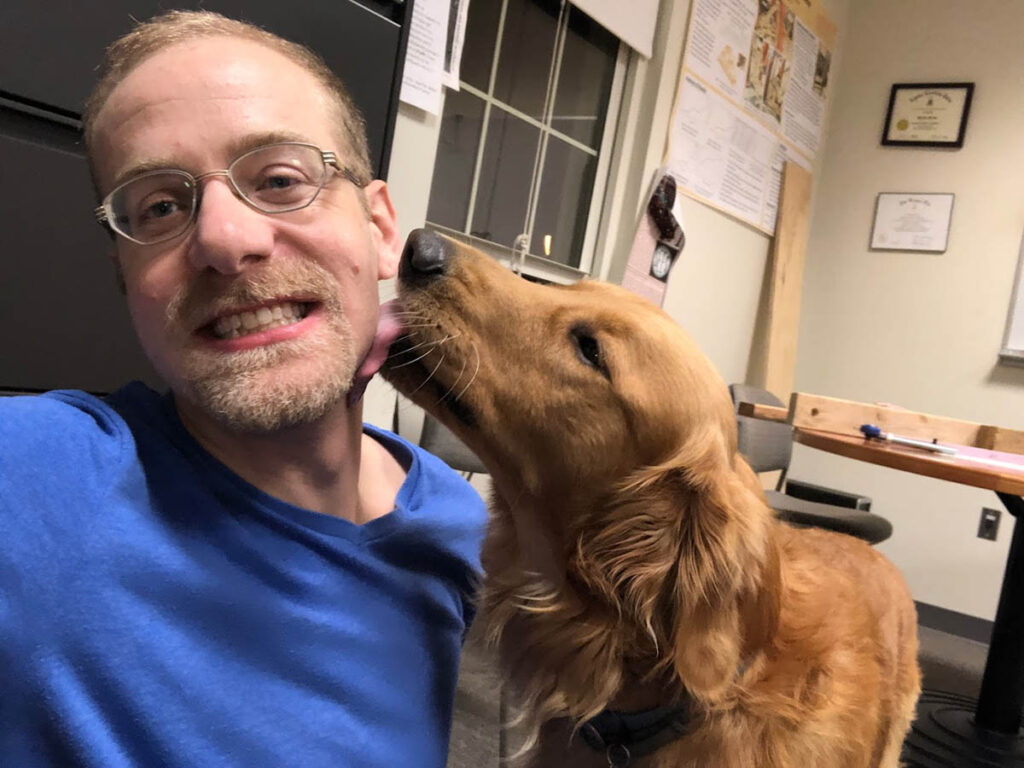Prof. Dave Mante smiles as his golden retriever Charlie licks his cheek. 