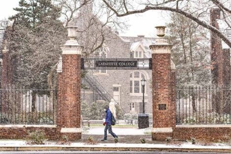 a student in a mask walks near a campus gateway as snow falls