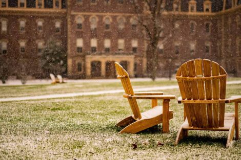 a light snow falls on Adirondack chairs on the Quad