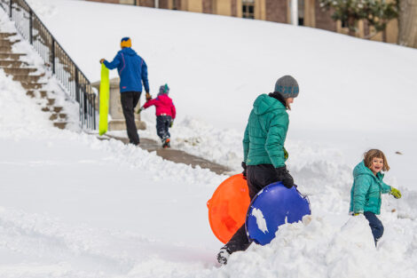 adults and children carry sleds toward the steps behind Pardee Hall