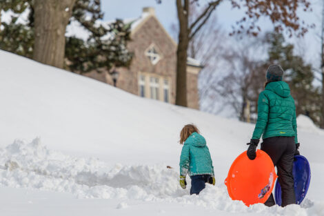 an adult and child stand with sleds with Farinon in the background