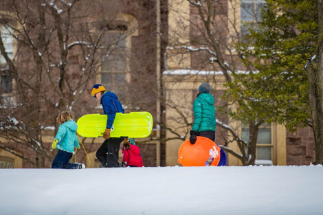 a family walks with sleds through the snow near Pardee Hall