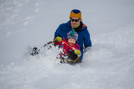 a father and child sled down a hill in the snow