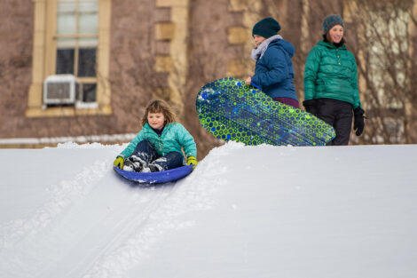 a young child sleds down a hill in the snow near Pardee Hall