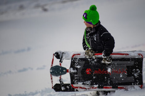 a young child carries a sled on campus in the snow