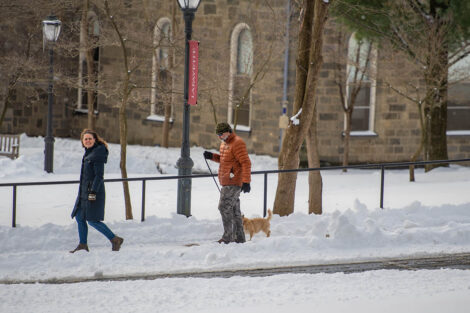 Two people walk their dog through a snow-covered campus
