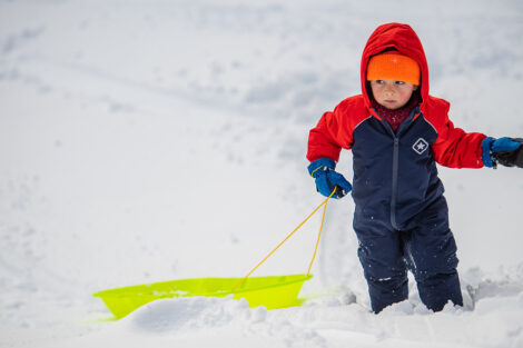 a young child drags a sled through the snow on campus