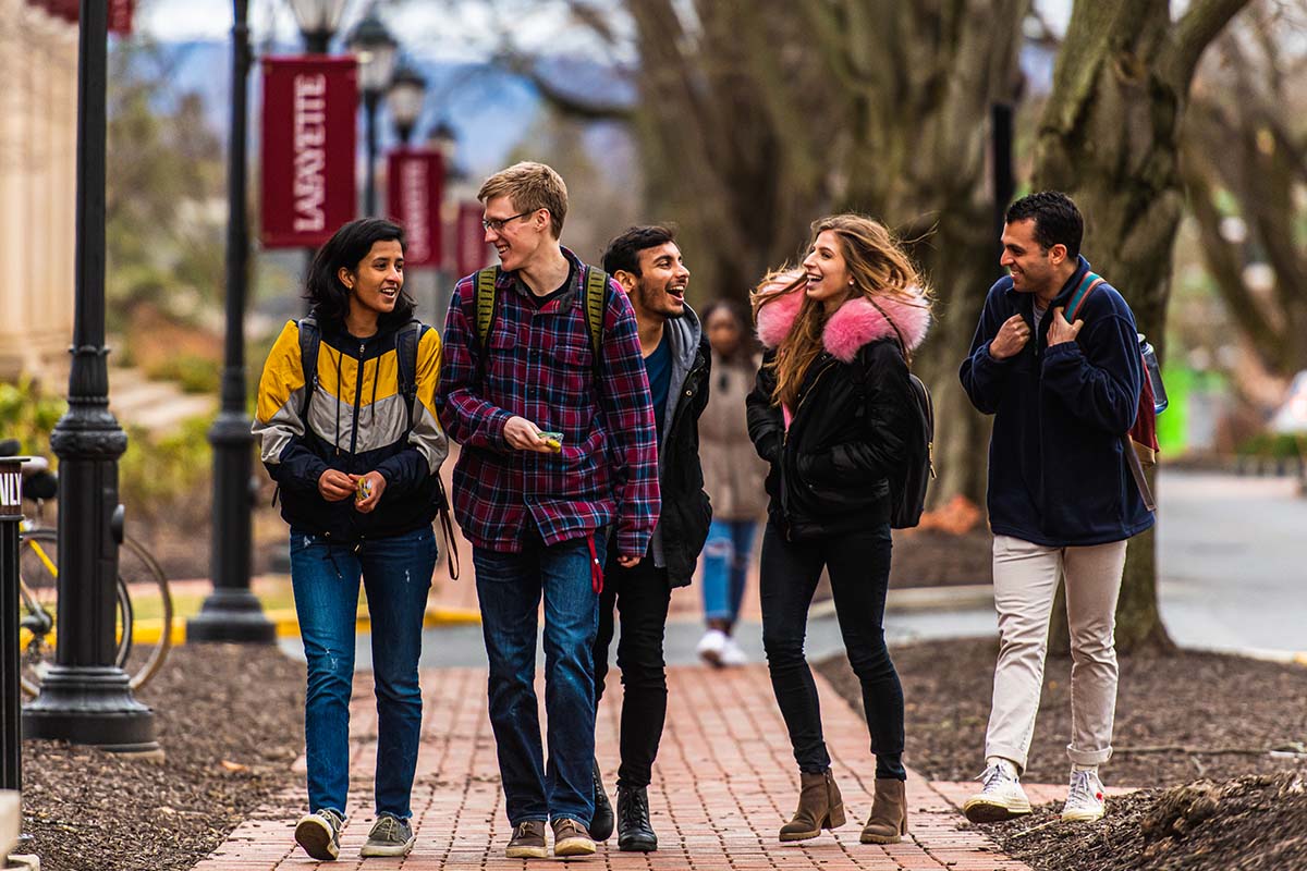 A group of 5 students talk while walking next to Markle Hall